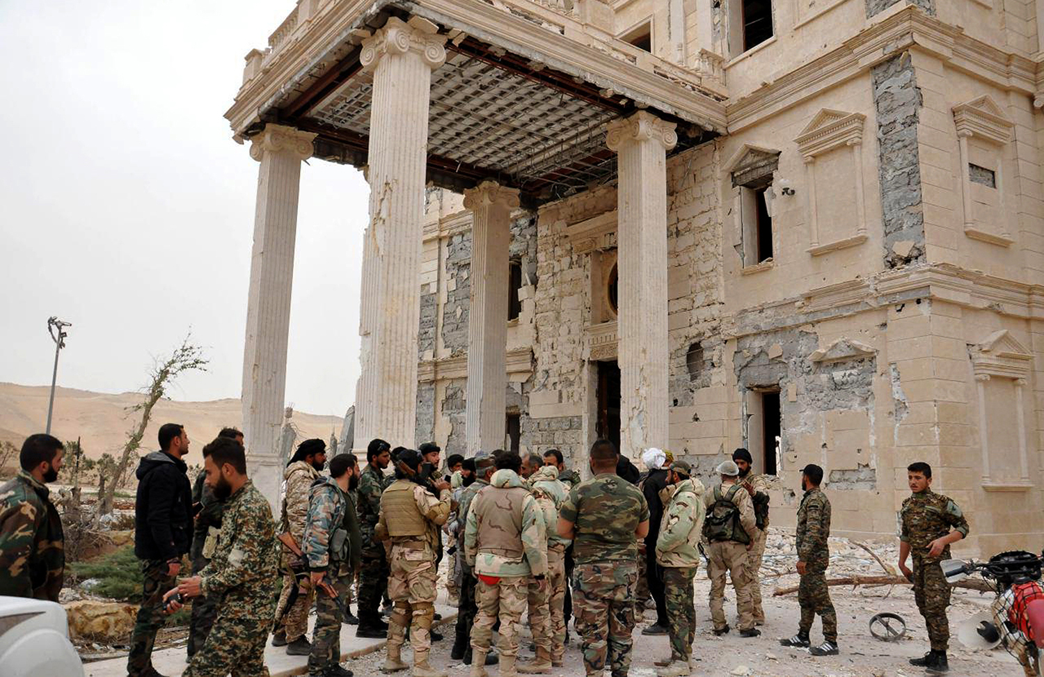 FILE -- In this file photo released March 24, 2016, by the Syrian official news agency SANA, Syrian government soldiers gather outside a damaged palace, in Palmyra, central Syria. Palmyra, the archaeological gem that Islamic State fighters retook Sunday, Dec. 11, 2016, from Syrian troops is a desert oasis surrounded by palm trees, and a UNESCO world heritage site, that boasts 2,000-year-old towering Roman-era colonnades and priceless artifacts. It is also a strategic crossroads linking the Syrian capital, Damascus, with the country's east and neighboring Iraq. (SANA via AP, File)