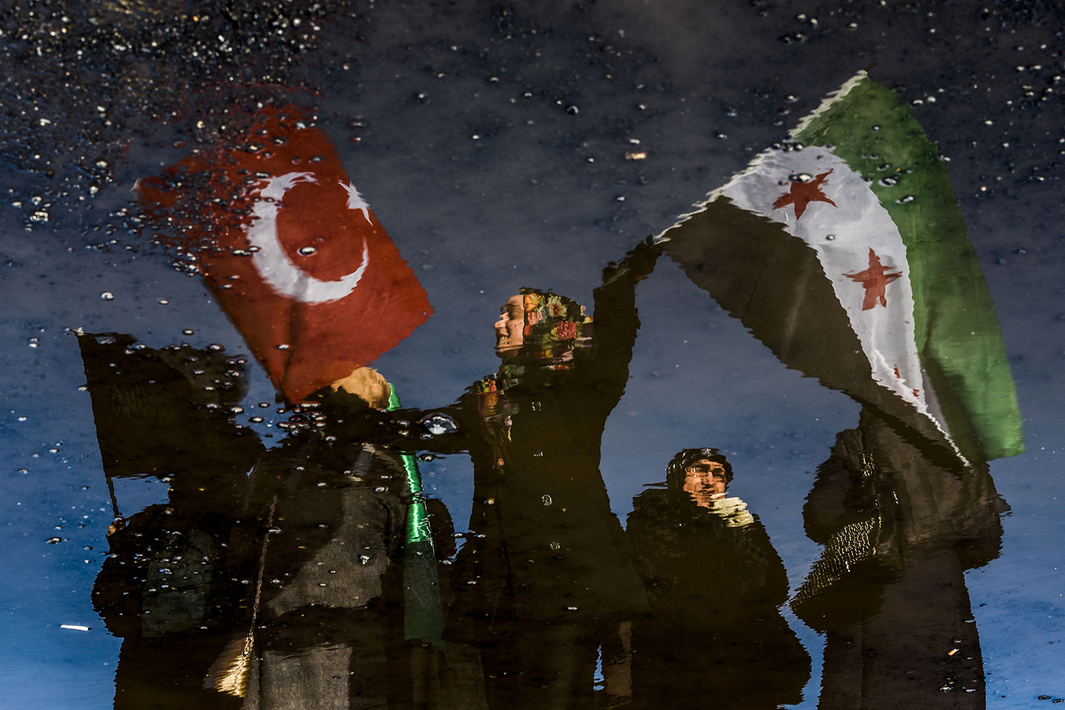 A reflection on waste liquid shows a woman wawing Turkish and Free Syrian flags as an aid convoy to Aleppo organized by IHH Humanitarian Relief Foundation is about to leave, on December 14, 2016 in Istanbul. Turkey's aid campaign for the besieged people of Aleppo continued with several nongovernmental organizations sending food, water and clothing. / AFP PHOTO / OZAN KOSE / TT / kod 444