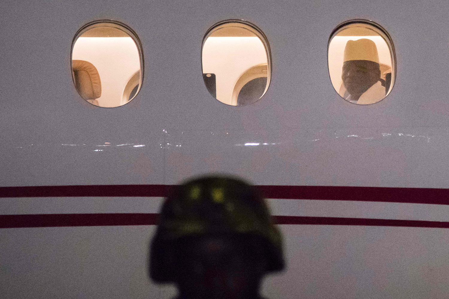 TOPSHOT - Former president Yaya Jammeh the Gambia's leader for 22 years, looks through the window from the plane as he leaves the country on 21 January 2017 in Banjul airport. Yahya Jammeh, the Gambia's leader for 22 years, flew out of the country on January 21, 2017 after declaring he would step down and hand power to President Adama Barrow, ending a political crisis. An AFP journalist at the airport saw Jammeh board an unmarked plane heading for an unspecified destination, seen off by a delegation of dignitaries and soldiers. / AFP PHOTO / STRINGER / TT / kod 444