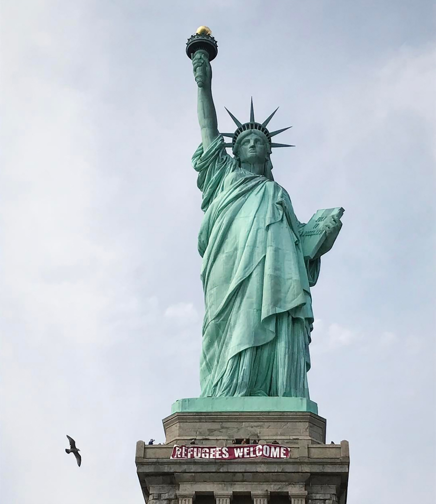 In this photo provided by VitÃ³ria Londero, a giant banner saying "Refugees Welcome" hangs on the pedestal of the Statue of Liberty, Tuesday, Feb. 21, 2017, in New York. National Park Service spokesman Jerry Willis says the banner was hung from the public observation deck at the top of the statue's pedestal Tuesday afternoon. (VitÃ³ria Londero via AP)