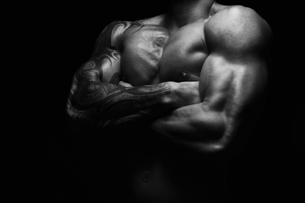 Athletic man's torso. Unrecognizable male fitness model show naked muscular body. Strong muscles and biceps. Studio shot on black background, monochrome, black and white. Bodybuilding concept